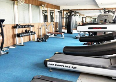 Modern gym interior with treadmills, dumbbells, weight machines, mirrors, and blue flooring in a spacious fitness center.