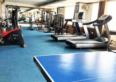 Modern gym interior with treadmills, dumbbells, weight machines, mirrors, and blue flooring in a spacious fitness center.