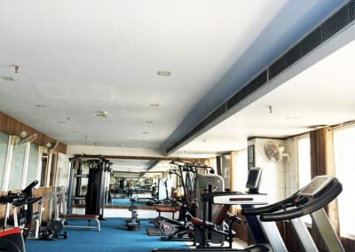 Modern gym interior with treadmills, dumbbells, weight machines, mirrors, and blue flooring in a spacious fitness center.