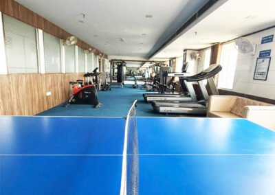 Modern gym interior with treadmills, dumbbells, weight machines, mirrors, and blue flooring in a spacious fitness center.